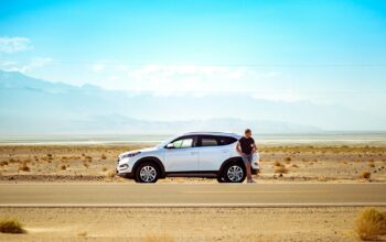 man standing beside white SUV near concrete road under blue sky at daytime